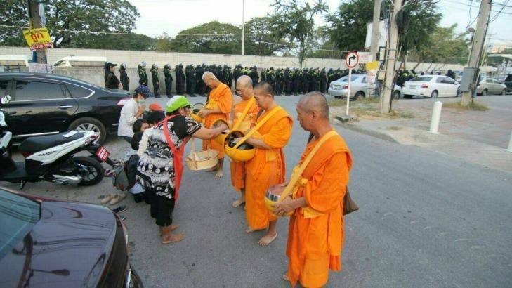 Monks at Thailand's largest Buddhist temple Wat Dhammakaya accept an offering while police line up in the background. Photo: Supplied