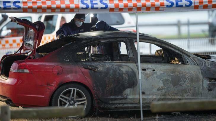 Police examine the burnt-out sedan at Olive Road Reserve. Photo: Jason South