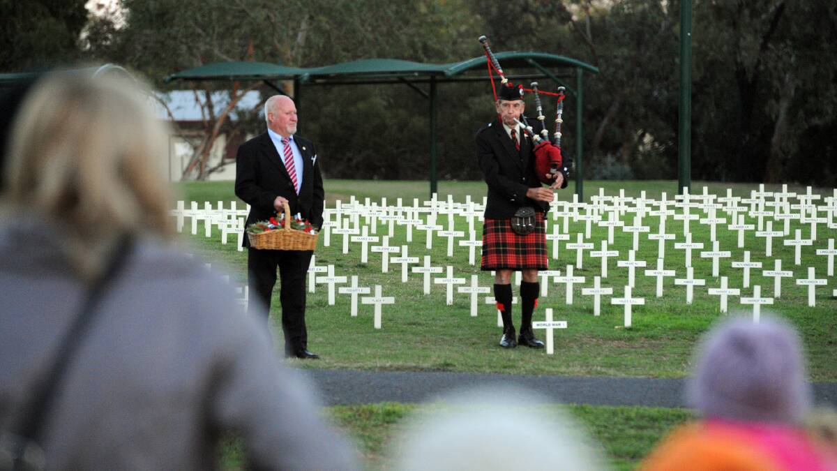 Peter Creek with poppies and Ron Abbott plays the bagpipes at Horsham Anzac Day dawn service. 