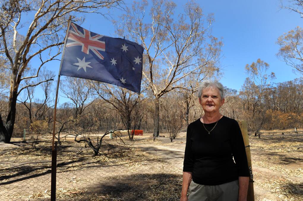 FIGHTING SPIRIT: Roses Gap resident Jean Swan with her Australian flag, a sign of hope and mateship against the burnt bushland beyond. Pictures: PAUL CARRACHER