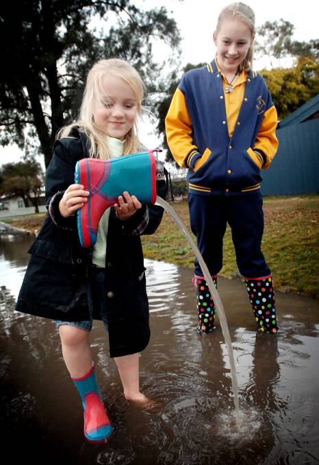 NEW EXPERIENCE: Brooke Loft, 5, and sister Kaitlyn Loft, 11, are not used to playing in puddles, let alone having to empty the water from their boots. The children were happy to play in the water as more than 50 millimetres of rain fell on the city on Monday. Picture: TIM HESTER