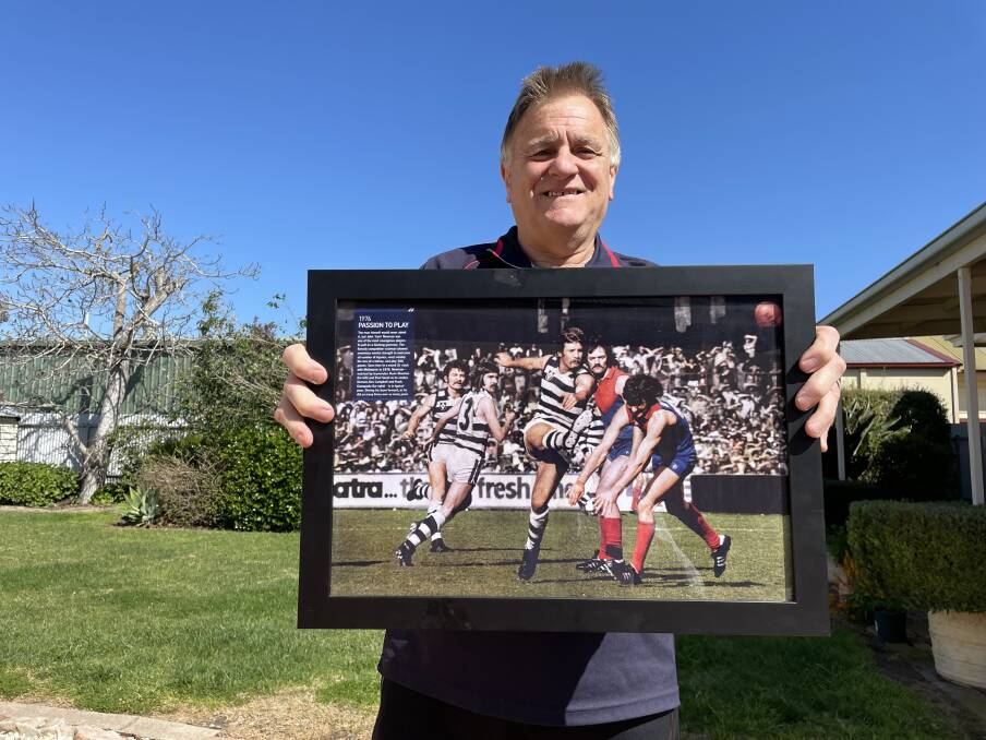 PRIDE: Passionate Dees man Frank Giampaolo holding a prized photo showing him in his Melbourne playing days attempting to smother the kick of Geelong legend Sam Newman. Picture: MATT HUGHES