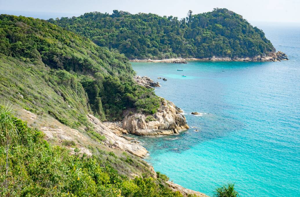 The green mountains of the Perhentian Islands run down to clear blue water.