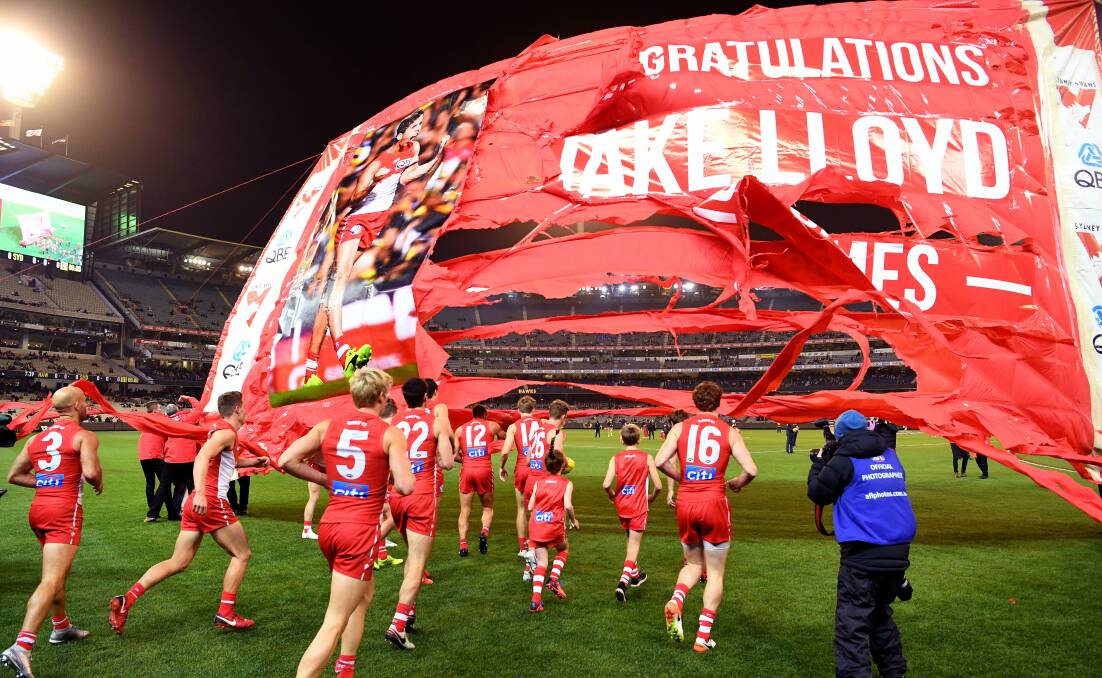 ONE HUNDRED: The Sydney Swans run through a banner marking Jake Lloyd's 100th game for the club on Friday night. Picture: AAP